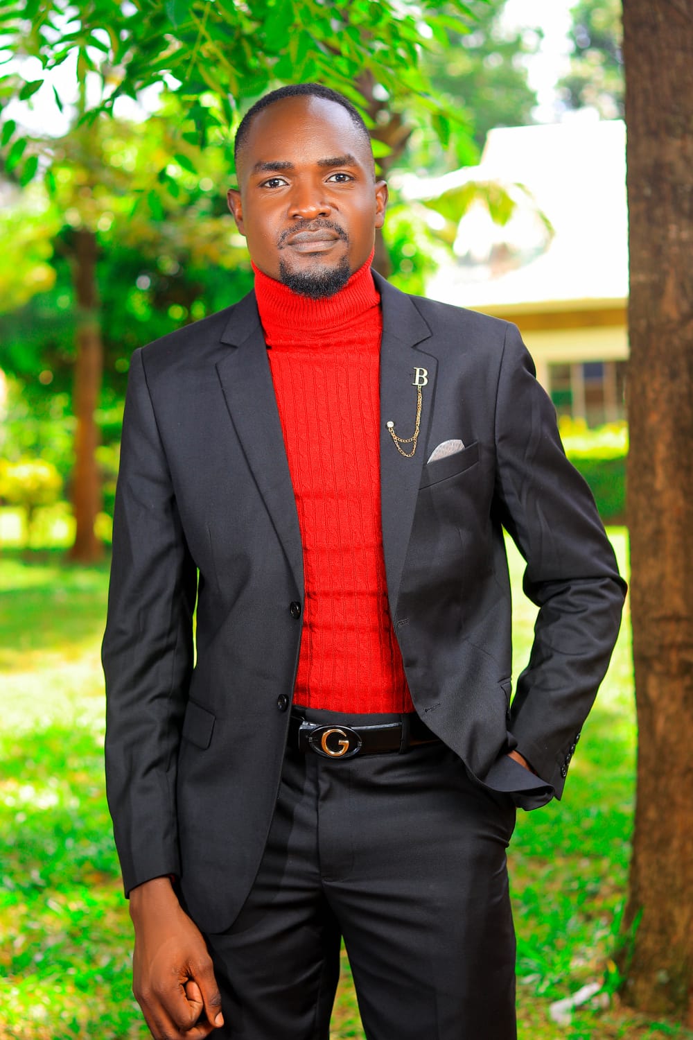 Dismus Nganyi in a black suit and red turtleneck, standing outdoors